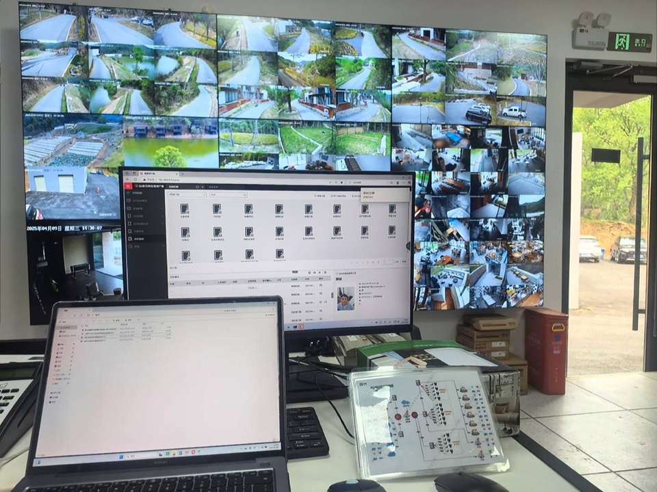 监控室里，大屏分路显示景区道路和室内画面，桌上放着拓扑图。